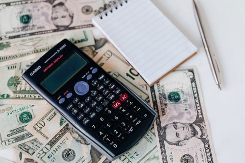 Photo of electronic calculator and notepad placed over United States dollar bills together with metallic pen for budget planning and calculation.